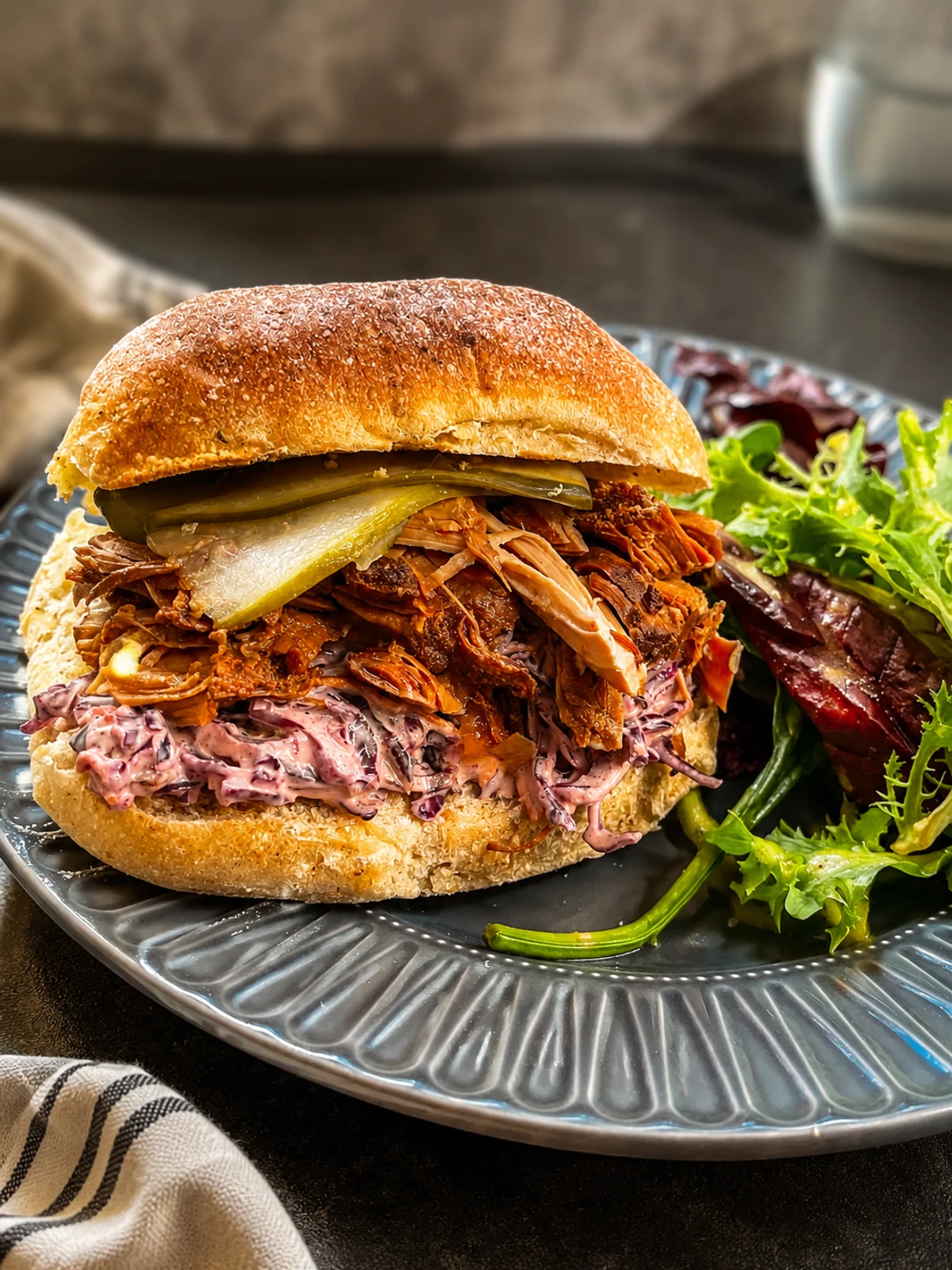 A pulled meat sandwich with pickles, slaw and a side salad